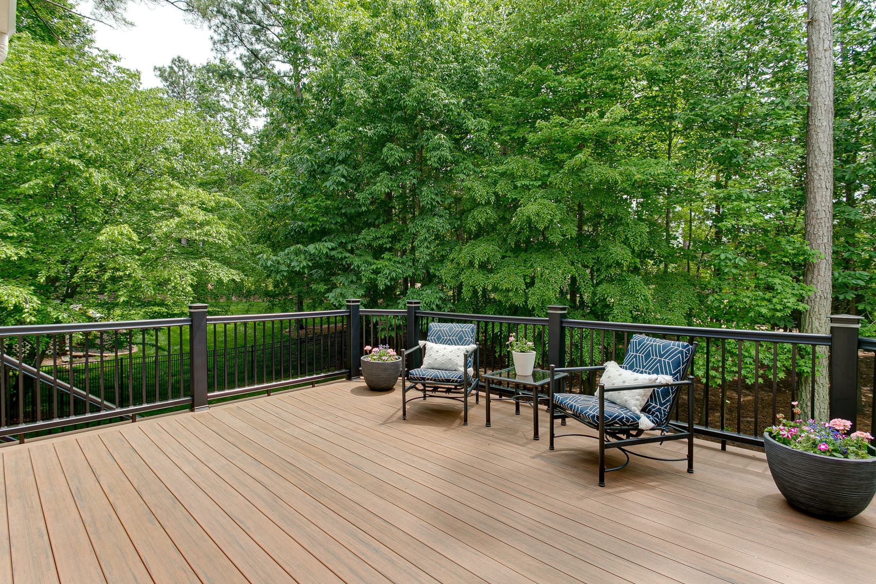 Composite deck with black metal railing and patio chairs among the trees
